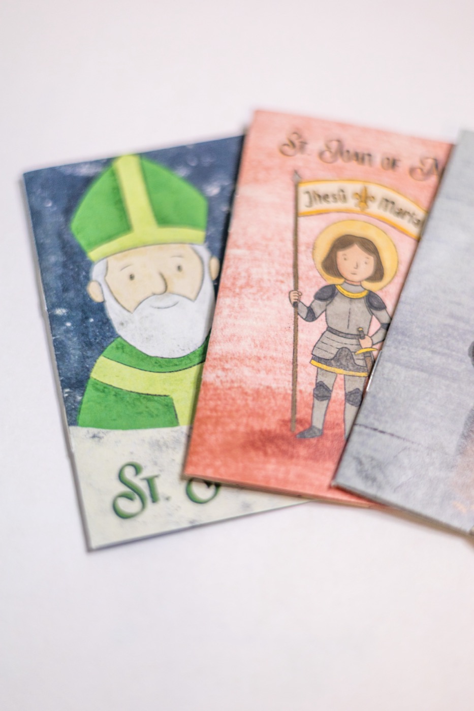 Hand-illustrated saint zine covers — St. Patrick, St. Joan of Arc, and St. Benedict