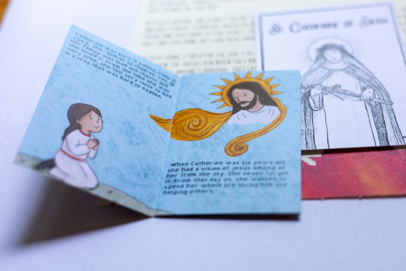 St. Catherine of Siena's hand-drawn zine, open to the spread where six-year-old Catherine sees Jesus smiling at her from the sky